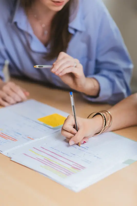 Close-up of a student's hand annotating her notebook, the founder in the background